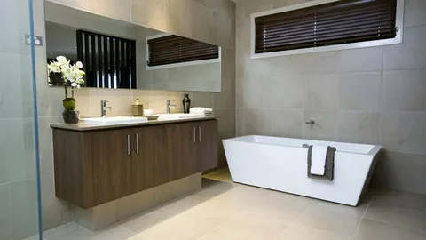 Best tile size for small bathroom showcased in a modern bathroom featuring a floating wood vanity with double sinks, a large mirror, a white freestanding bathtub, and beige tiled walls and floors.