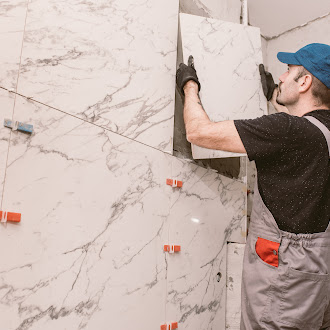A worker in a blue cap tile installation large marble tiles on a wall using tile spacers for alignment.
