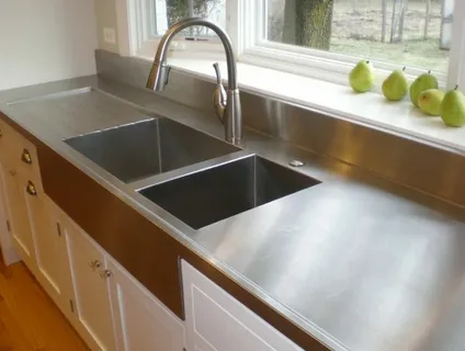 A stainless steel double-basin farmhouse sink with a gooseneck faucet on white cabinetry, showcasing the best countertop material options in a modern kitchen design.
