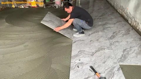 Flooring installer creating a tile installation design by fitting marble-look tile over ridged adhesive during a home renovation.